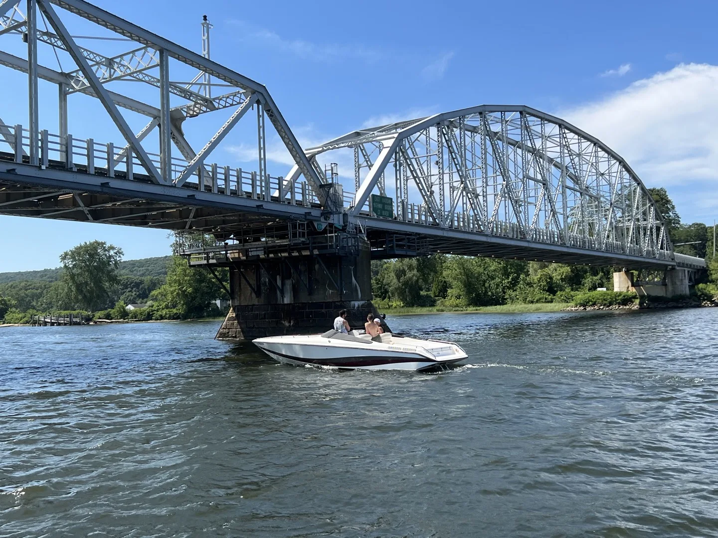 A powerboat on the Connecticut River passing under the East Haddam Swing Bridge, beside the River's Edge Home Center showroom in Haddam, CT